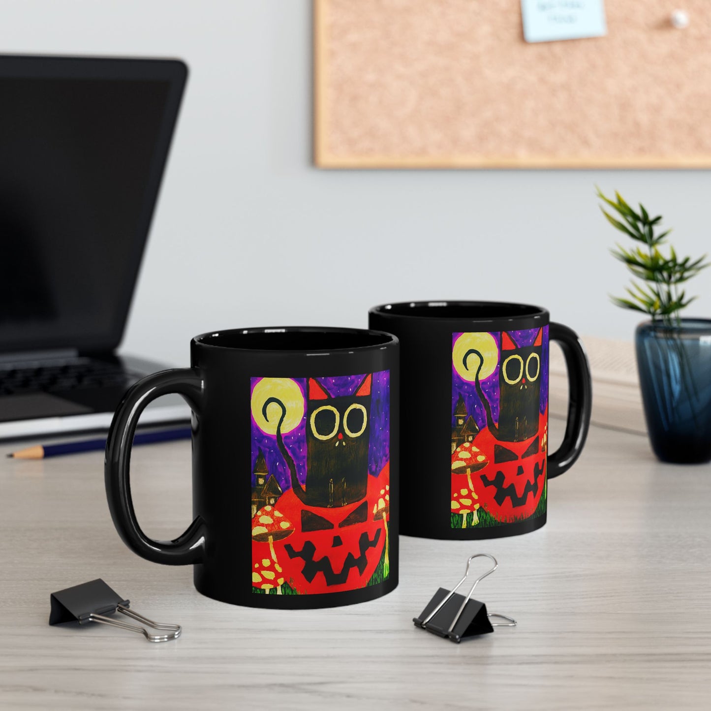 Two matching Halloween-themed mugs on a desk beside a laptop and a plant.